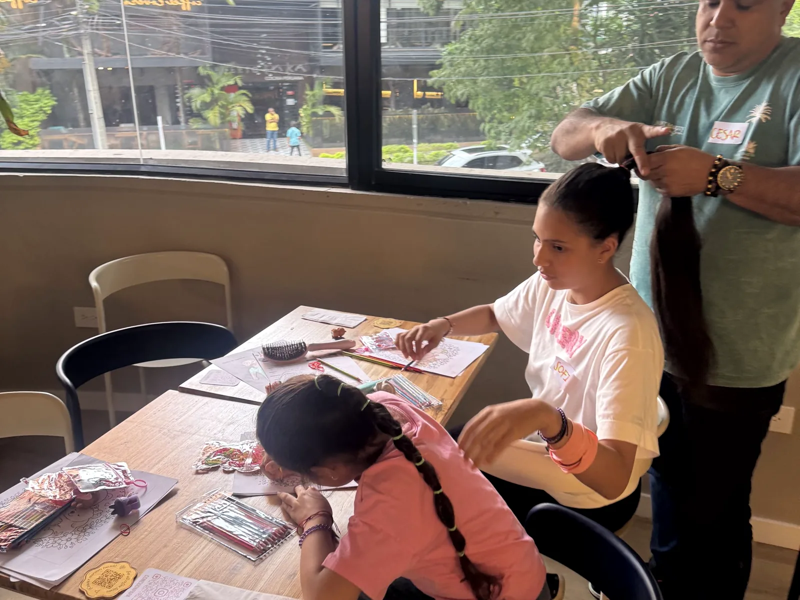 Un papá participa en el taller de trenzas mientras las niñas disfrutan una actividad creativa